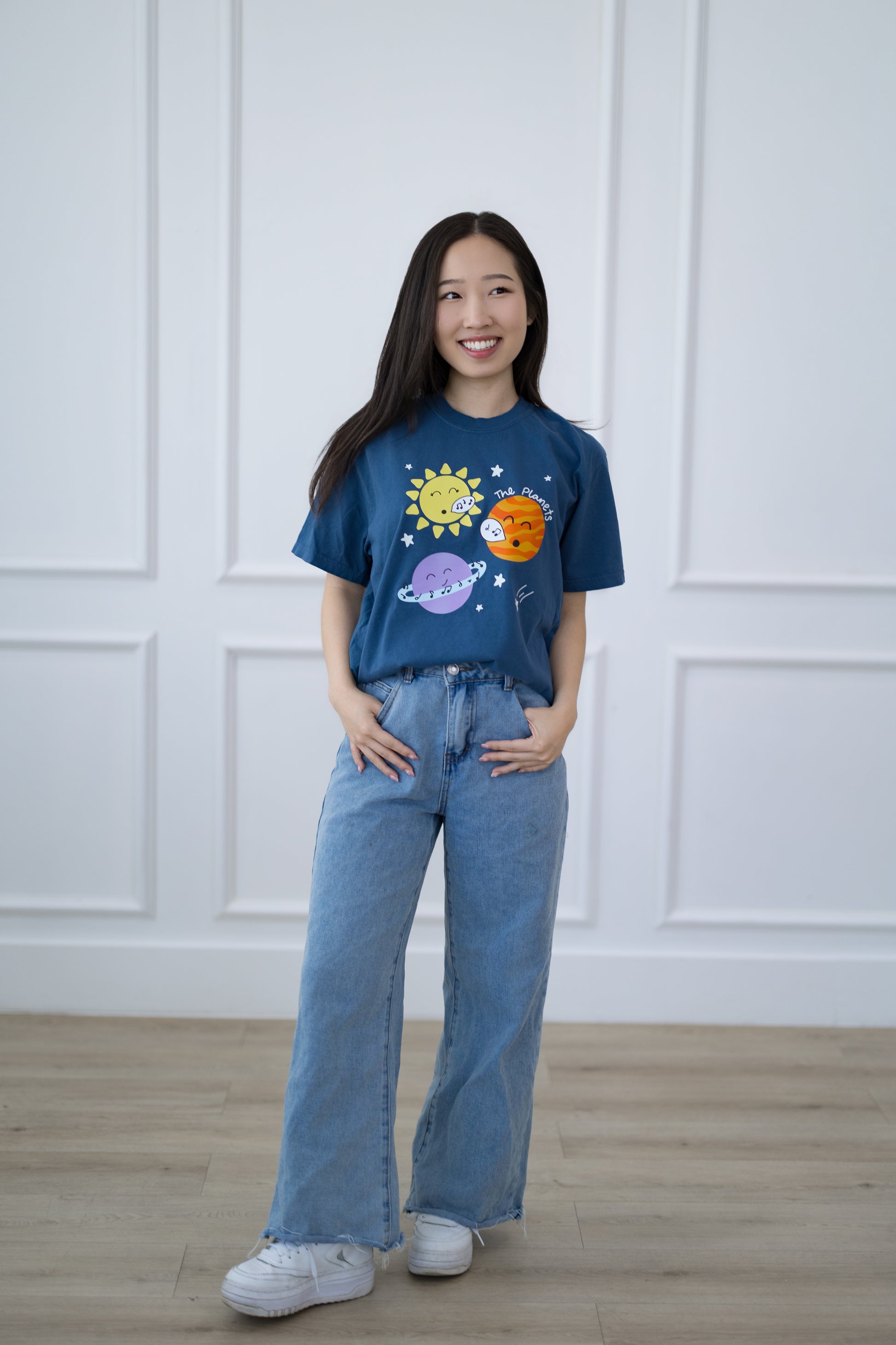 Person wearing a blue t-shirt with space-themed graphics against a white paneled wall.