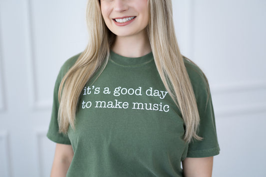Person wearing a green t-shirt with 'it's a good day to make music' text.