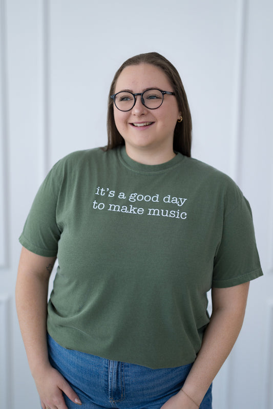 Person wearing a green t-shirt with text, standing against a white paneled wall.