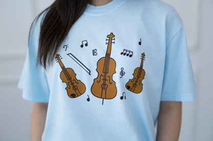 Light blue t-shirt with brown violin and cello illustrations and music notes on a plain background