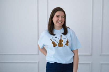 Person wearing a light blue t-shirt with musical instrument designs against a white paneled wall.
