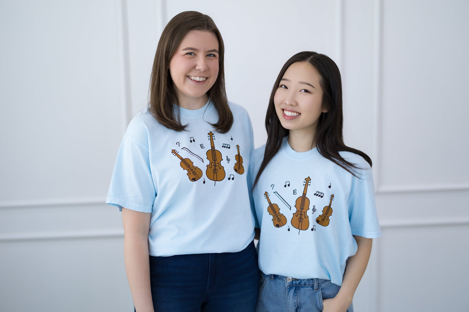 Two people wearing light blue t-shirts with musical instrument designs against a white background