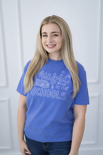 Person wearing a blue t-shirt with 'Music Belongs in Our Schools' text against a white background