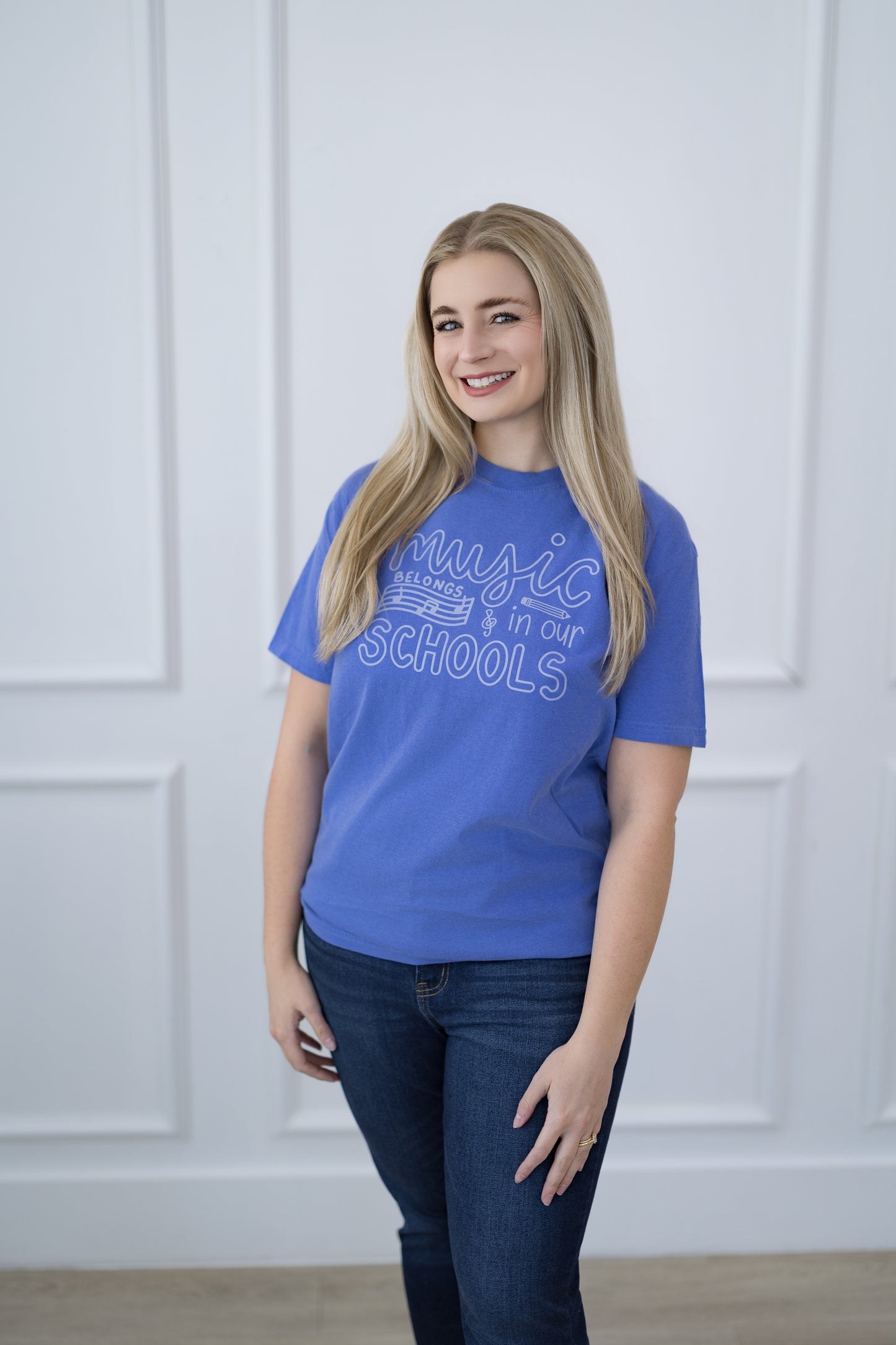 Woman wearing a blue t-shirt with text standing against a white paneled wall.