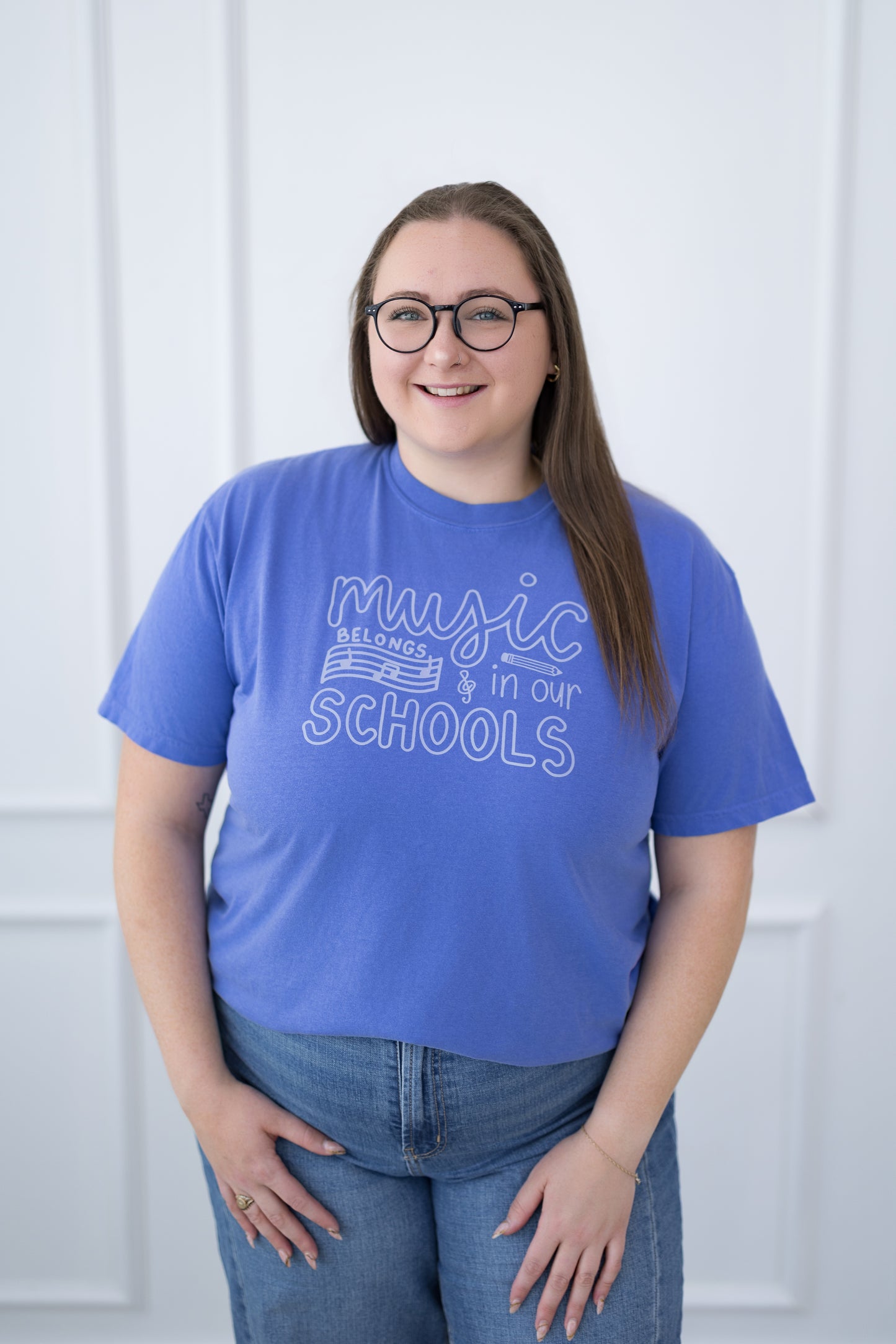 Person wearing a blue t-shirt with 'music belongs in our schools' text, standing against a white background.