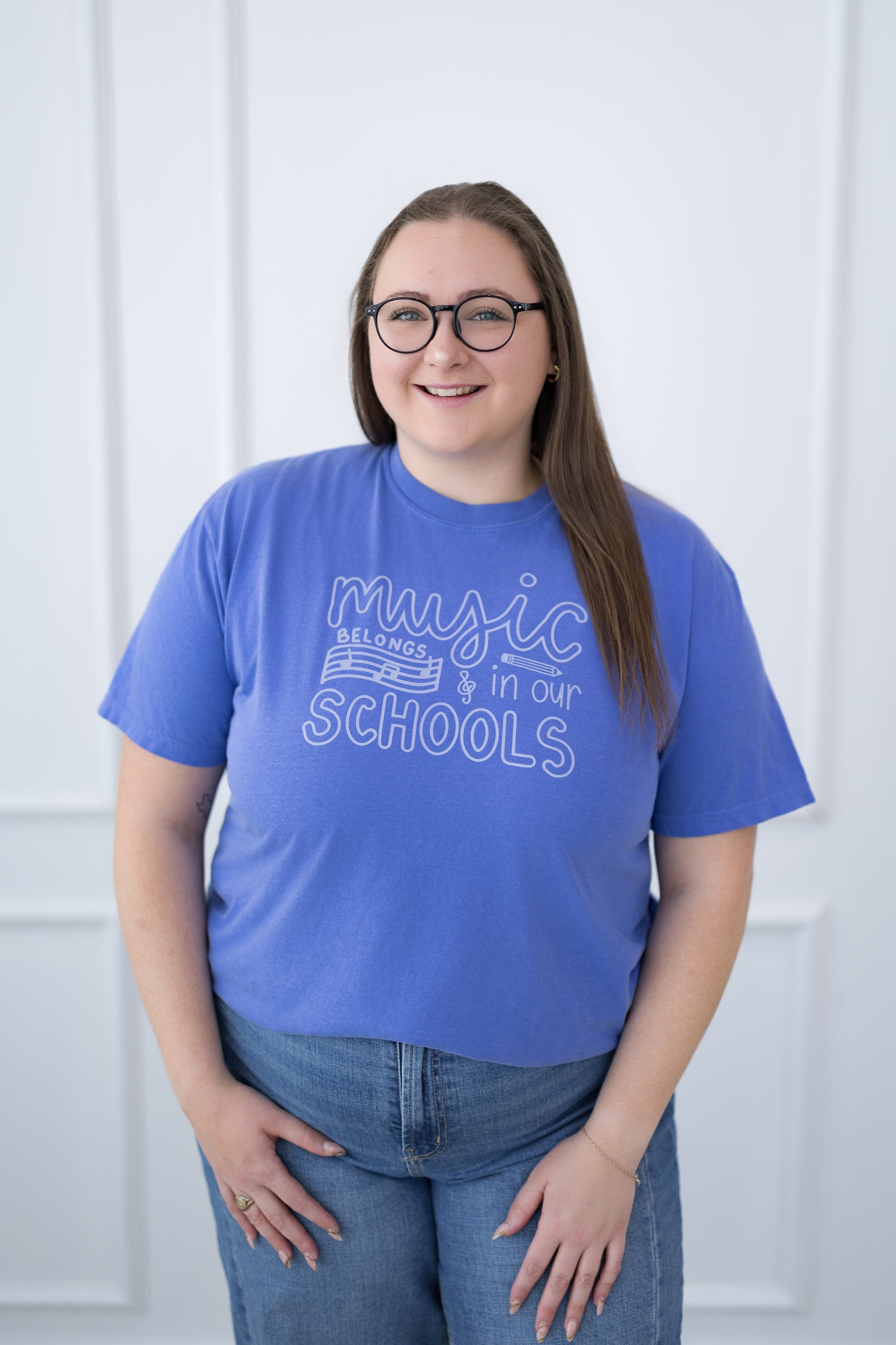 Person wearing a blue t-shirt with 'music belongs in our schools' text, standing against a white background.