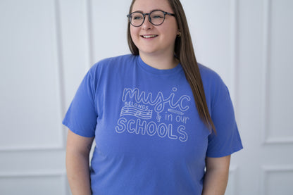 Person wearing a blue t-shirt with 'music belongs in our schools' text against a white background
