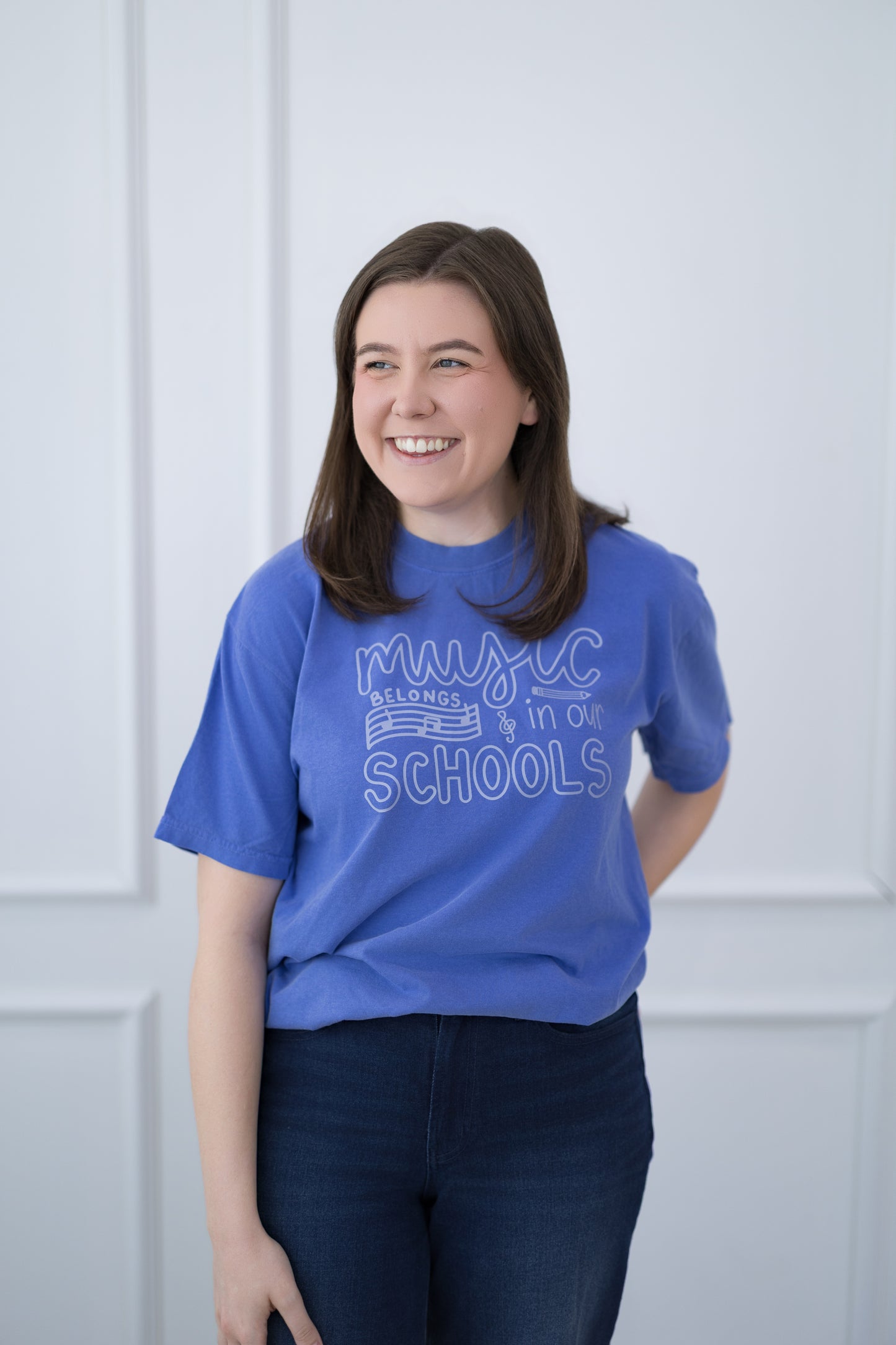 Person wearing a blue t-shirt with text, standing against a light-colored wall.