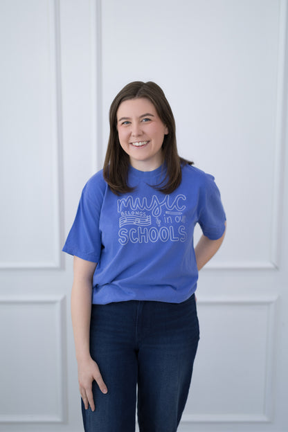 Person wearing a blue t-shirt with text standing against a white paneled wall.