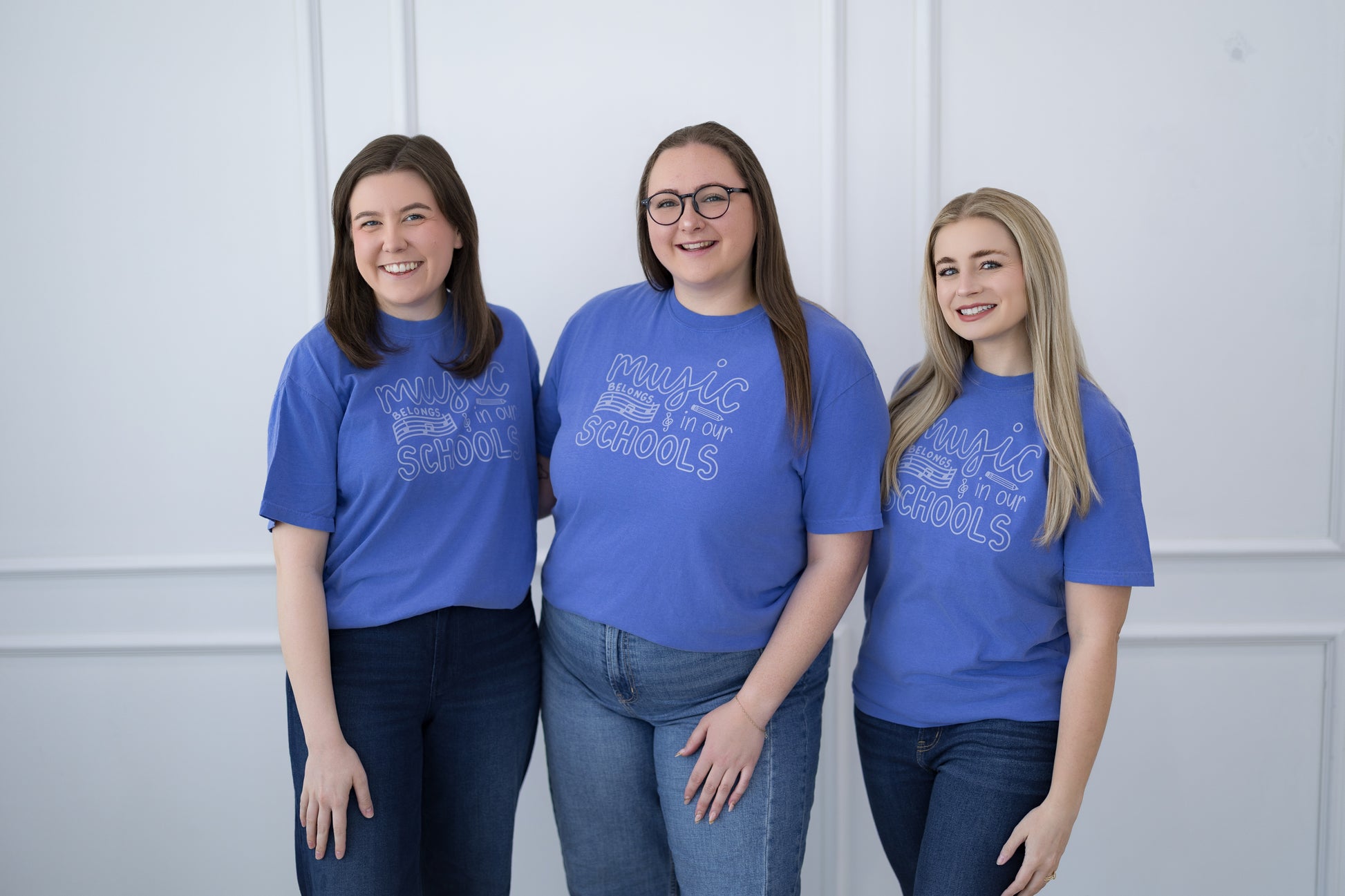 Three women wearing blue t-shirts with text standing against a white wall.
