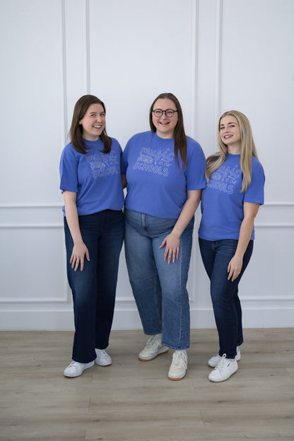 Three women wearing matching blue t-shirts standing against a white wall.