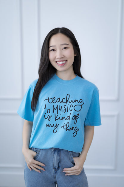 Person wearing a blue t-shirt with text, standing against a light-colored wall.