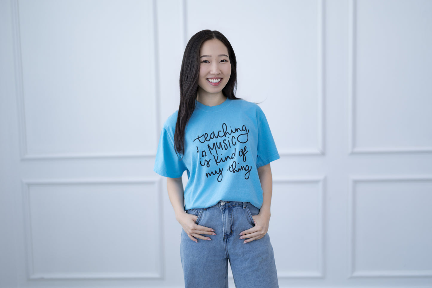 Woman wearing a blue t-shirt with text standing against a white paneled wall
