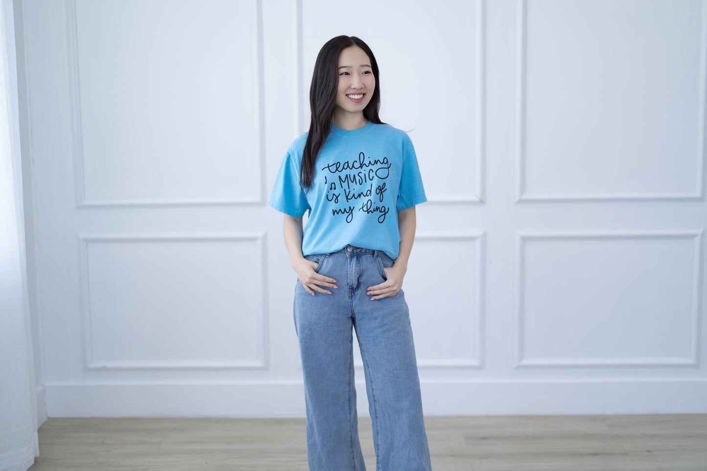 Woman wearing a blue t-shirt with text standing against a white paneled wall.