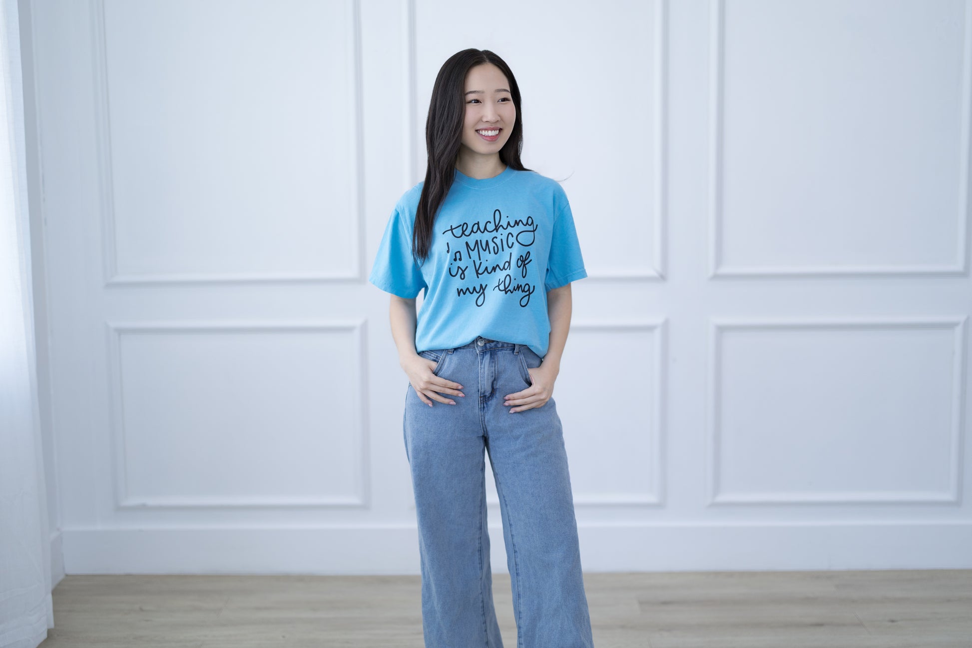 Woman wearing a blue t-shirt with text standing against a white paneled wall.