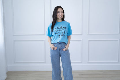 Woman wearing a blue t-shirt with text standing against a white paneled wall.