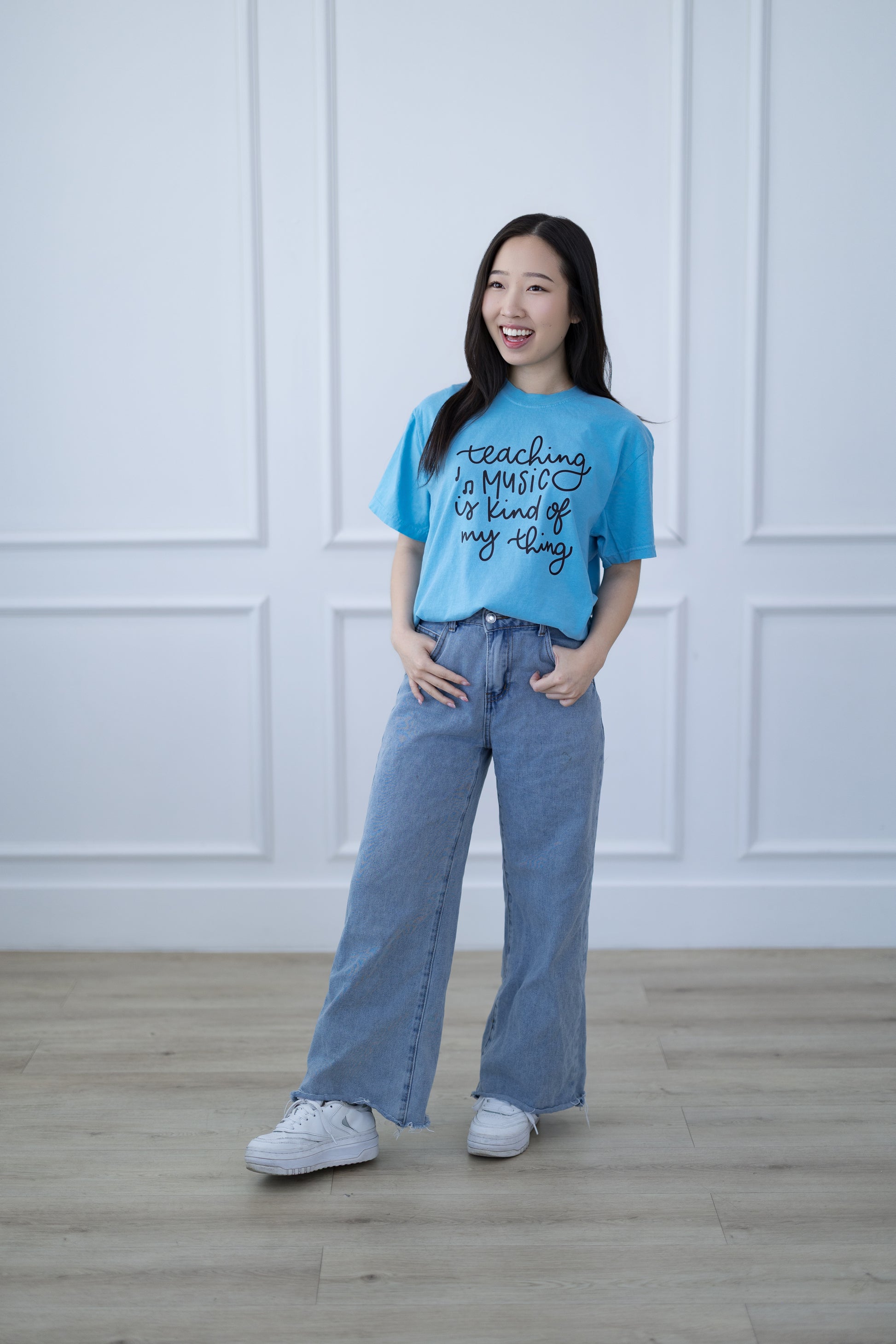 Woman wearing a blue t-shirt and jeans standing in a room with white paneled walls.