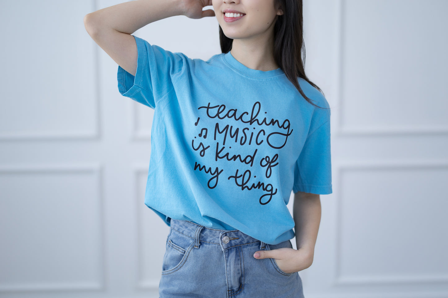 Person wearing a blue t-shirt with 'Teaching music is kind of my thing' text against a light background