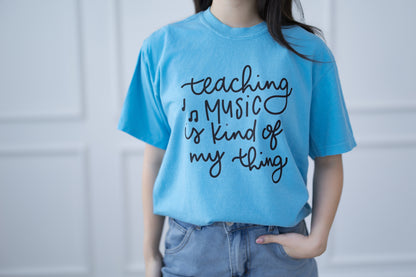 Person wearing a blue t-shirt with 'teaching music is kind of my thing' text.