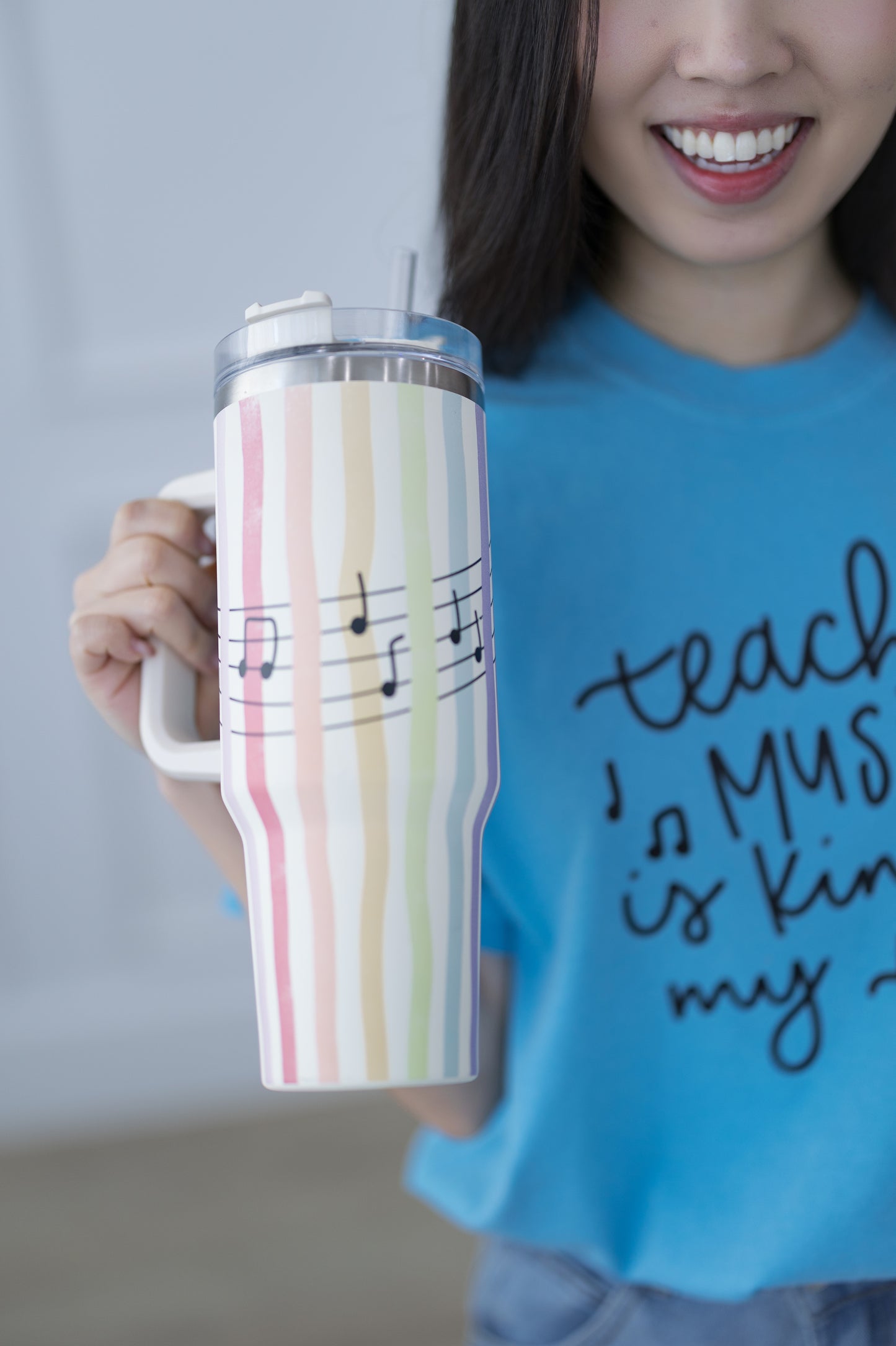 Person holding a striped tumbler with musical notes, wearing a blue shirt with text.