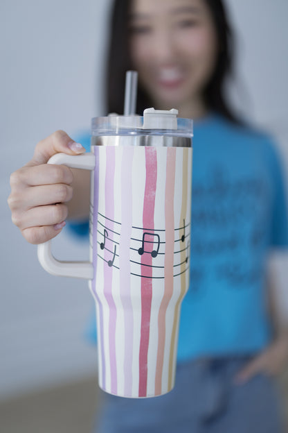 Person holding a striped tumbler with musical notes, blurred background