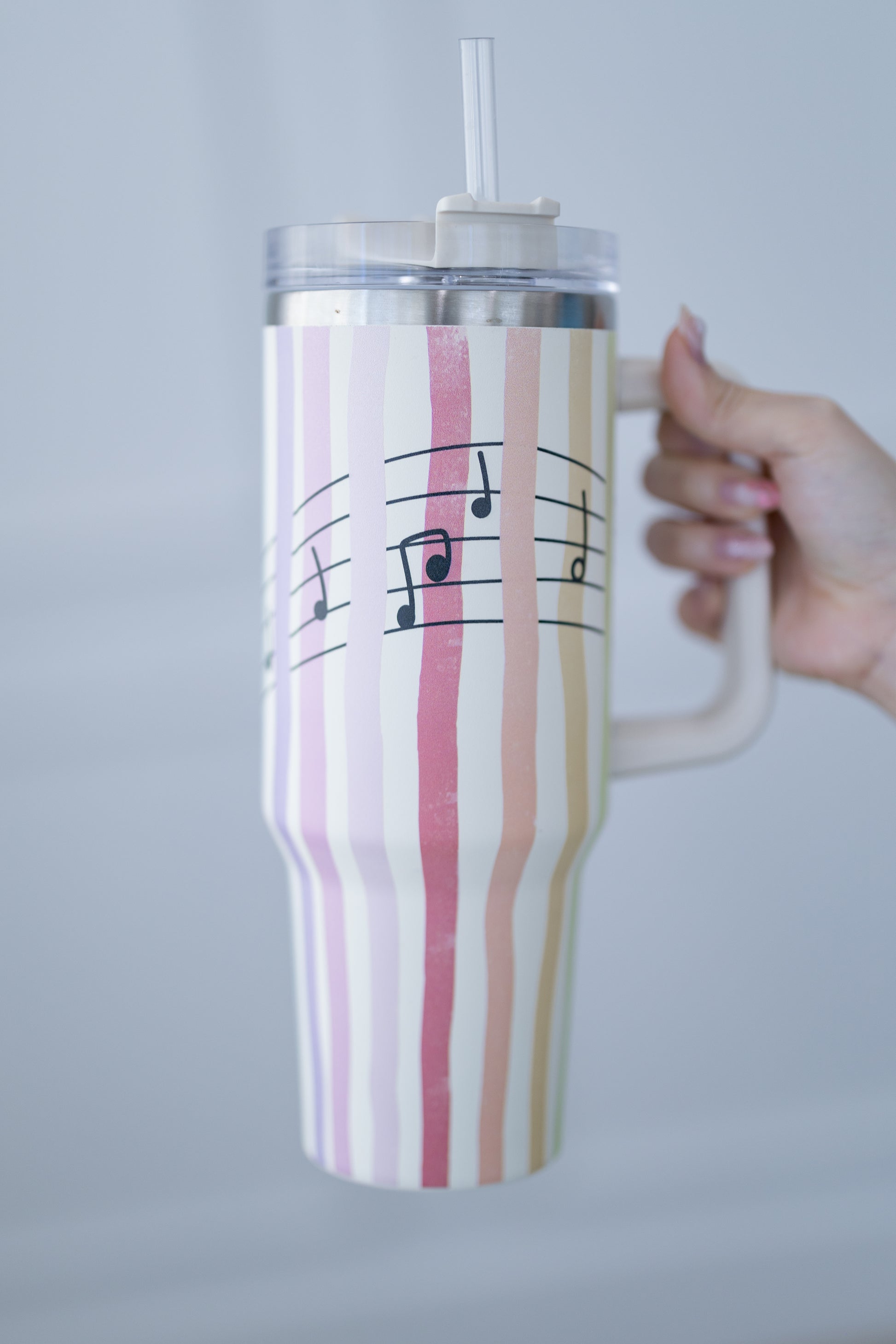 Striped mug with musical notes held by a hand against a gray background