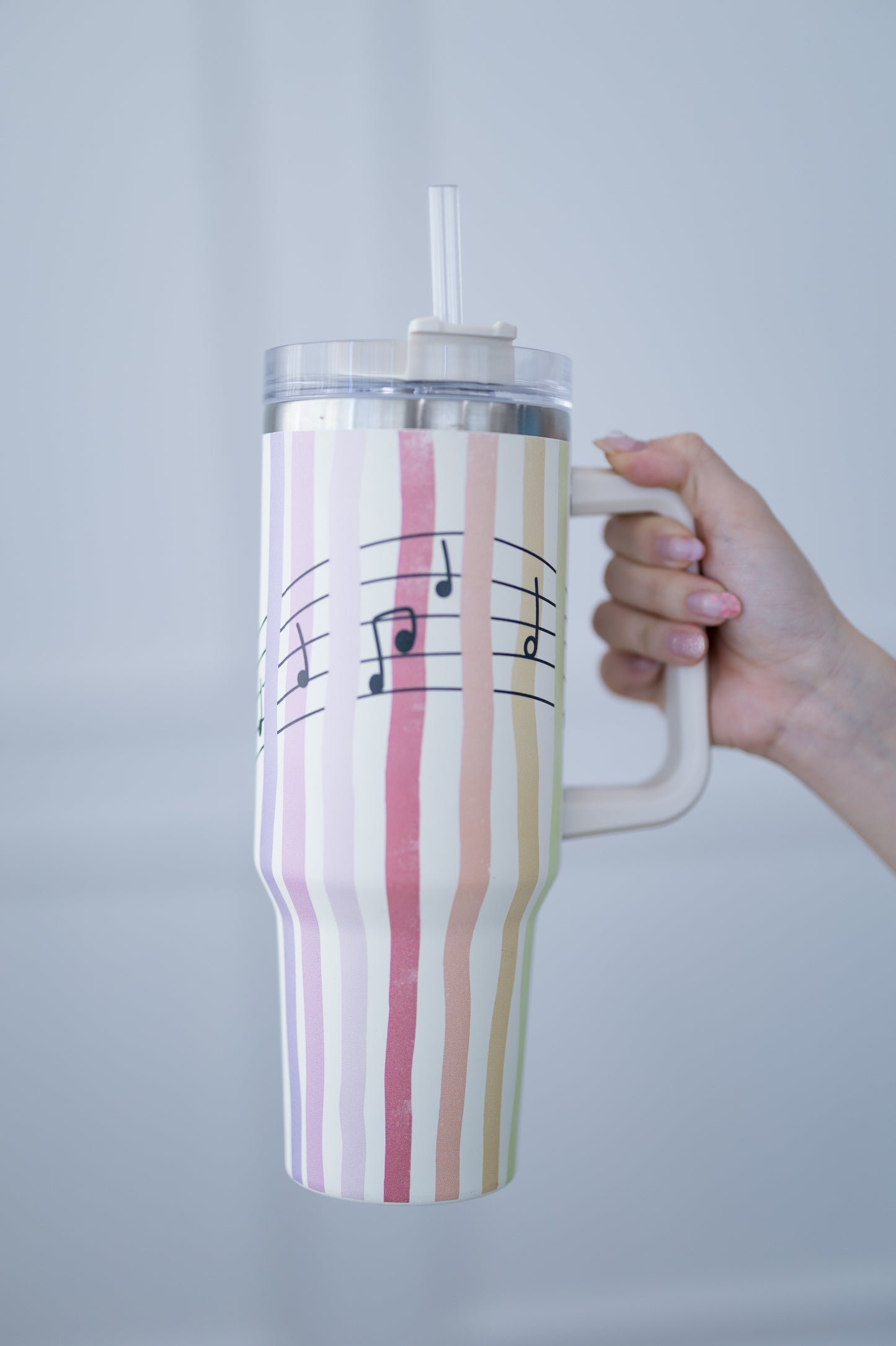 Striped tumbler with musical notes held by a hand against a plain background
