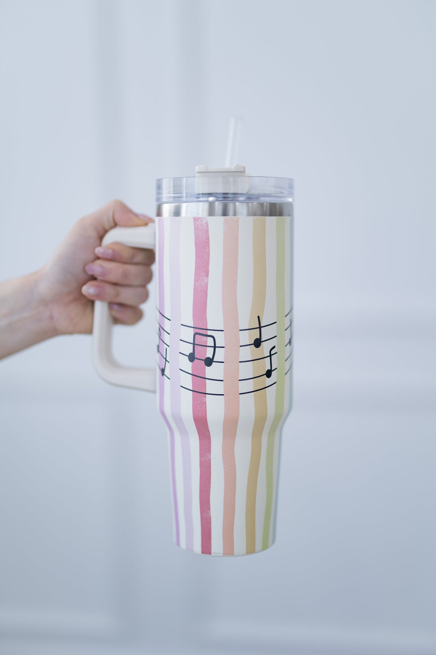 Tumbler with striped design and music notes held by a hand against a light background