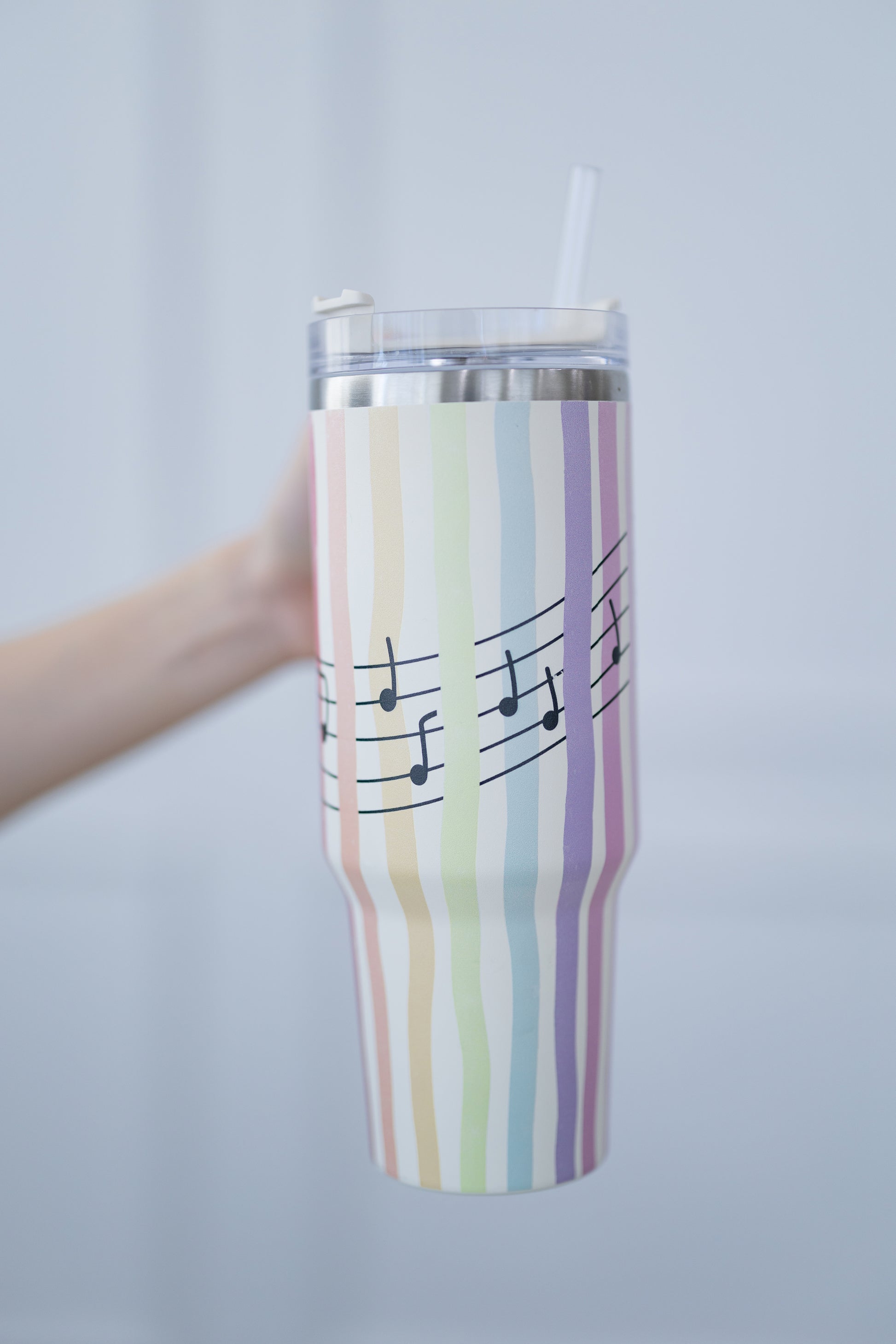 Tumbler with striped design and musical notes held against a plain background
