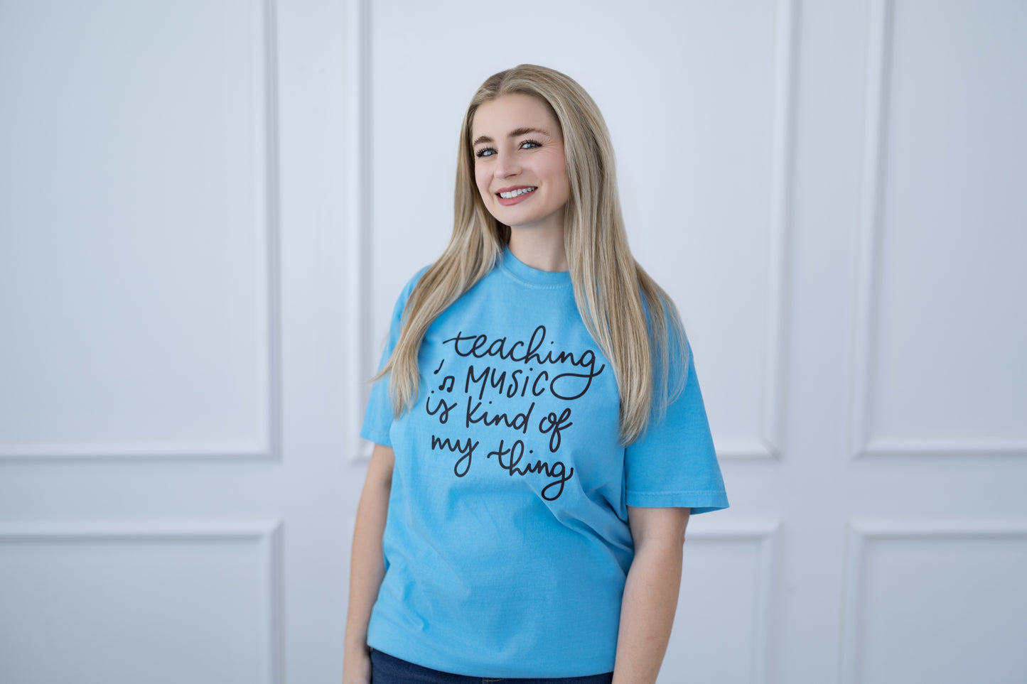 Person wearing a blue t-shirt with text, standing against a light-colored paneled wall.