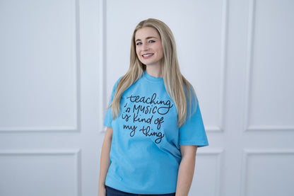 Person wearing a blue t-shirt with text, standing against a light-colored paneled wall.