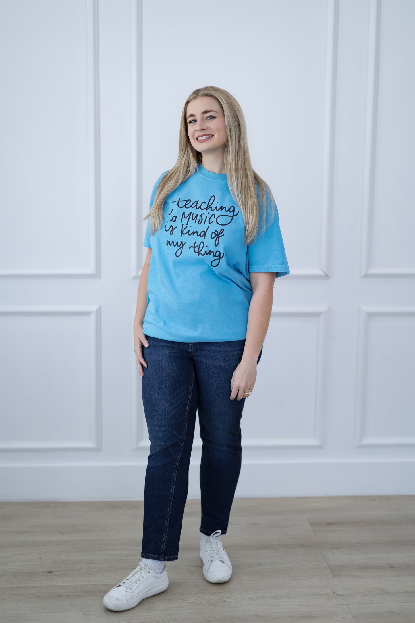 Person wearing a blue t-shirt with text, standing against a white paneled wall.