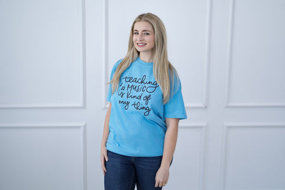 Woman wearing a blue t-shirt with text, standing against a white paneled wall.