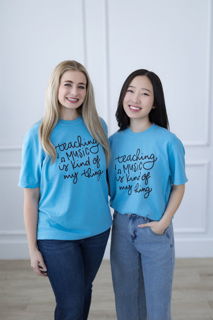 Two people wearing blue t-shirts with text, standing against a white wall.