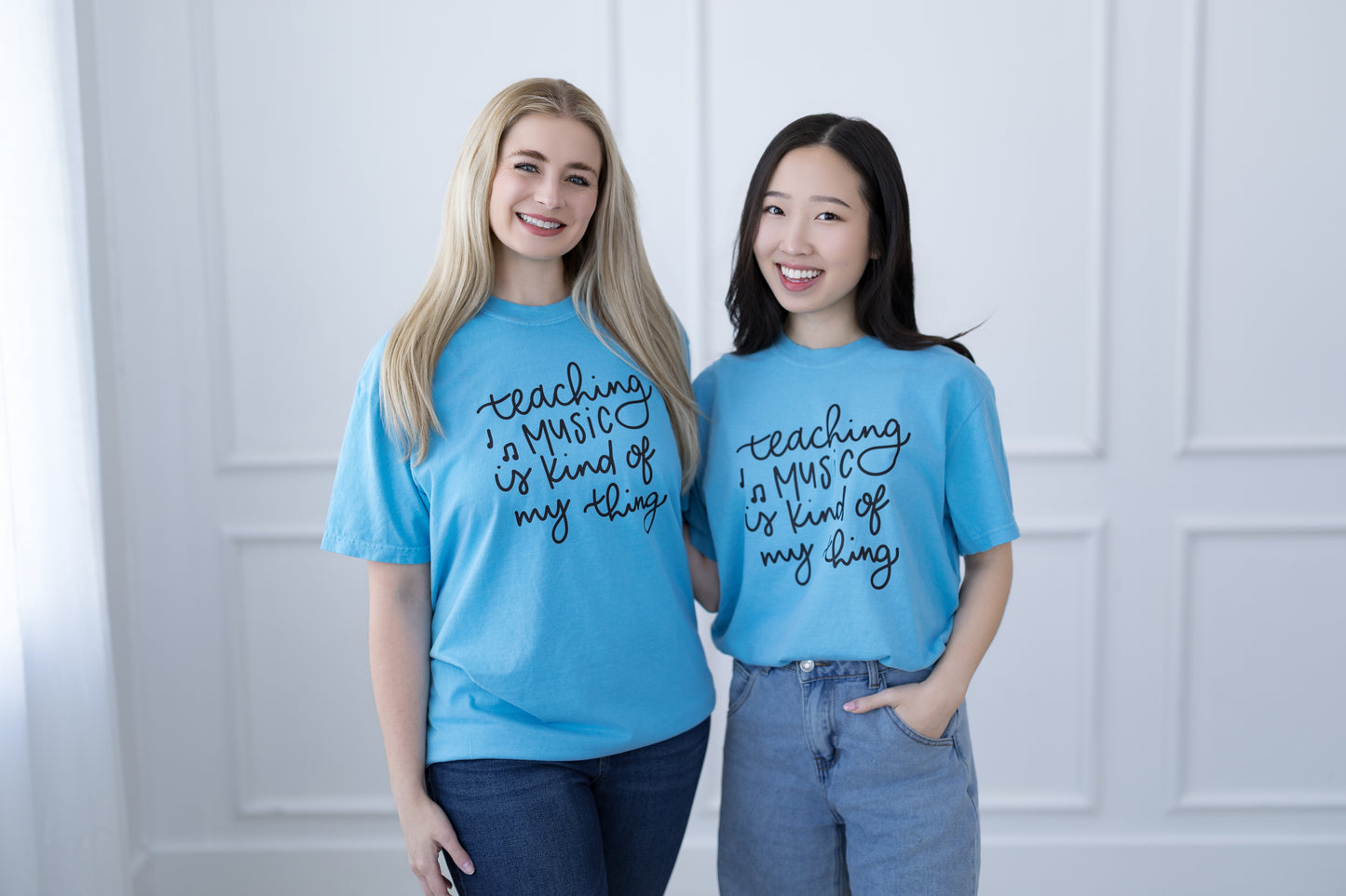 Two people wearing blue t-shirts with text, standing against a white wall.