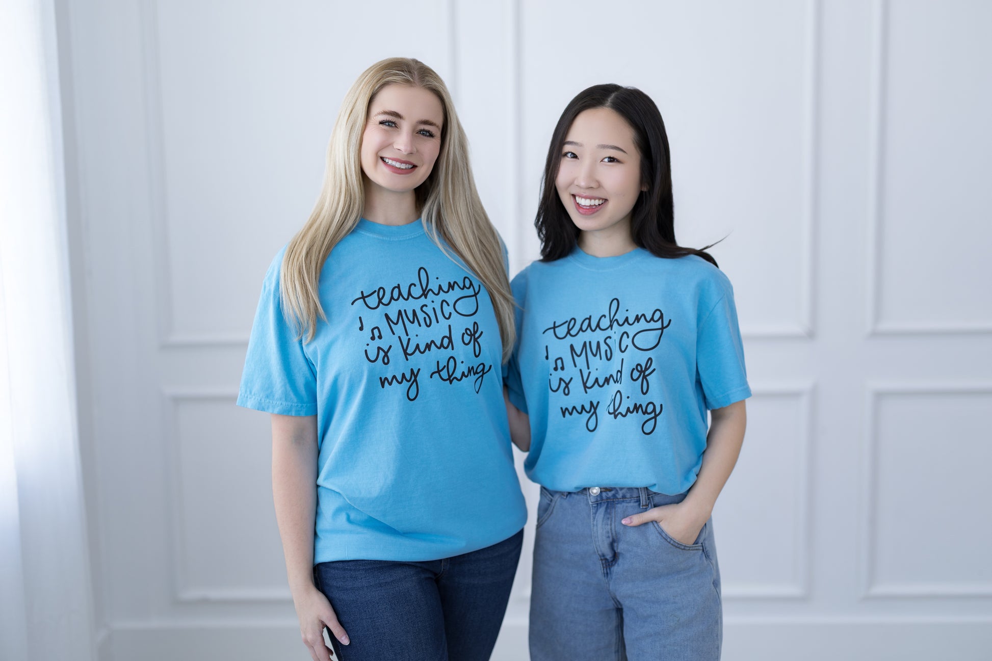 Two people wearing blue t-shirts with text, standing against a white wall.
