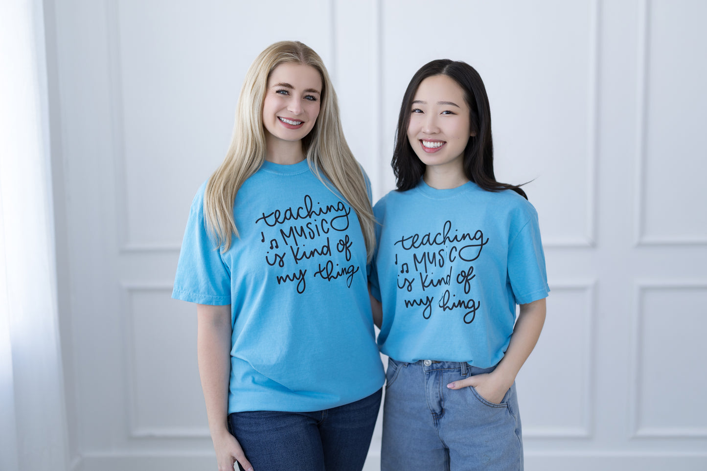 Two people wearing blue t-shirts with text standing against a white paneled wall.