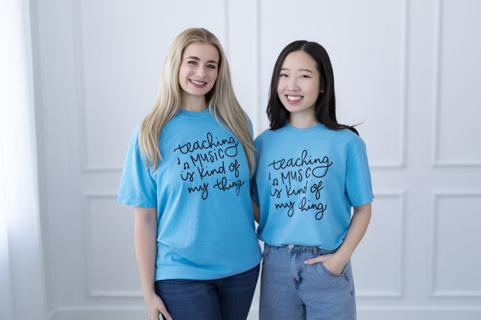 Two people wearing blue t-shirts with text standing against a white paneled wall.