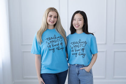 Two people wearing blue t-shirts with text standing against a white paneled wall.
