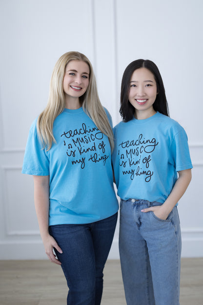 Two people wearing matching blue t-shirts with text, standing against a white wall.