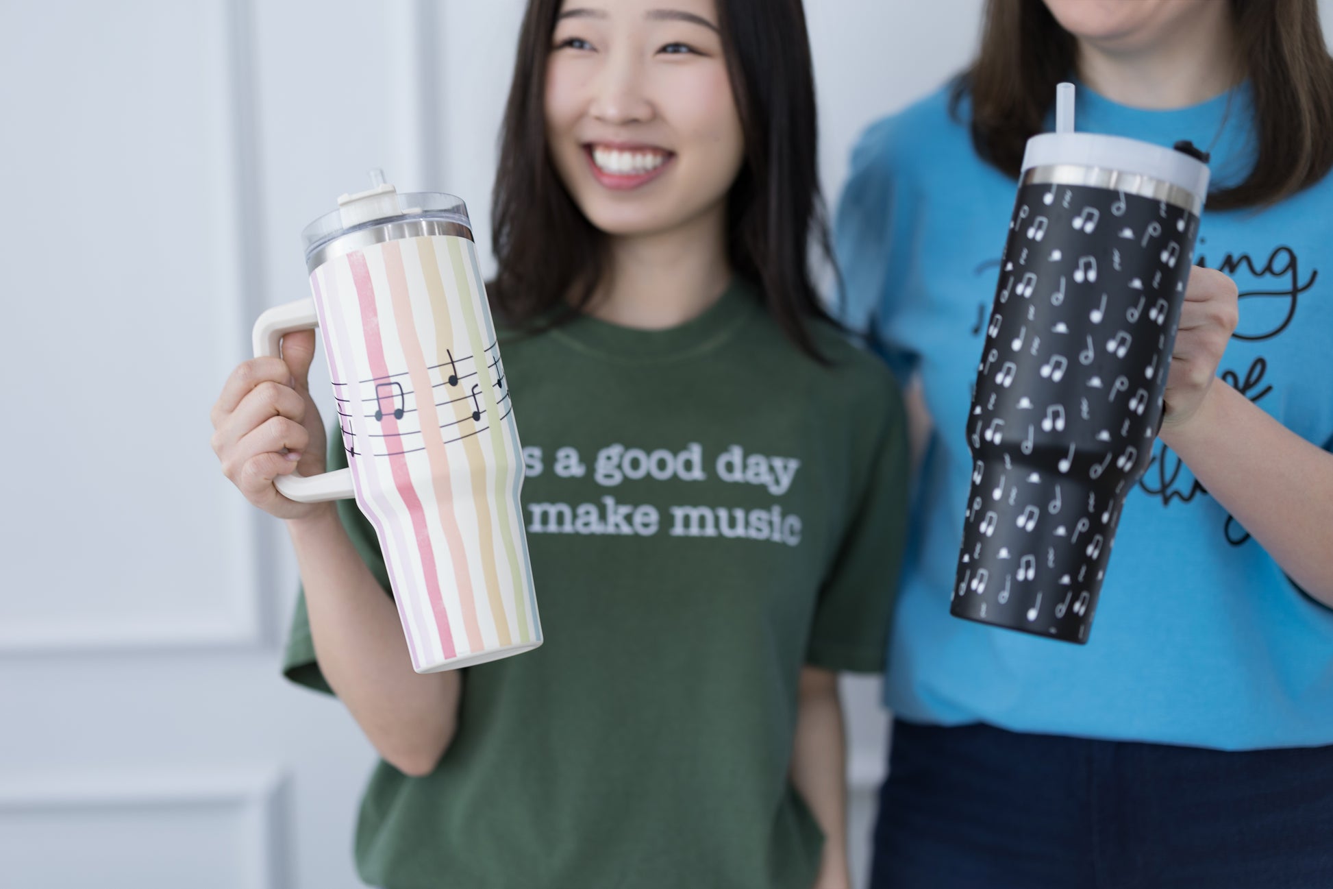 Two people holding tumblers with music-themed designs, one in a green shirt and the other in a blue shirt.