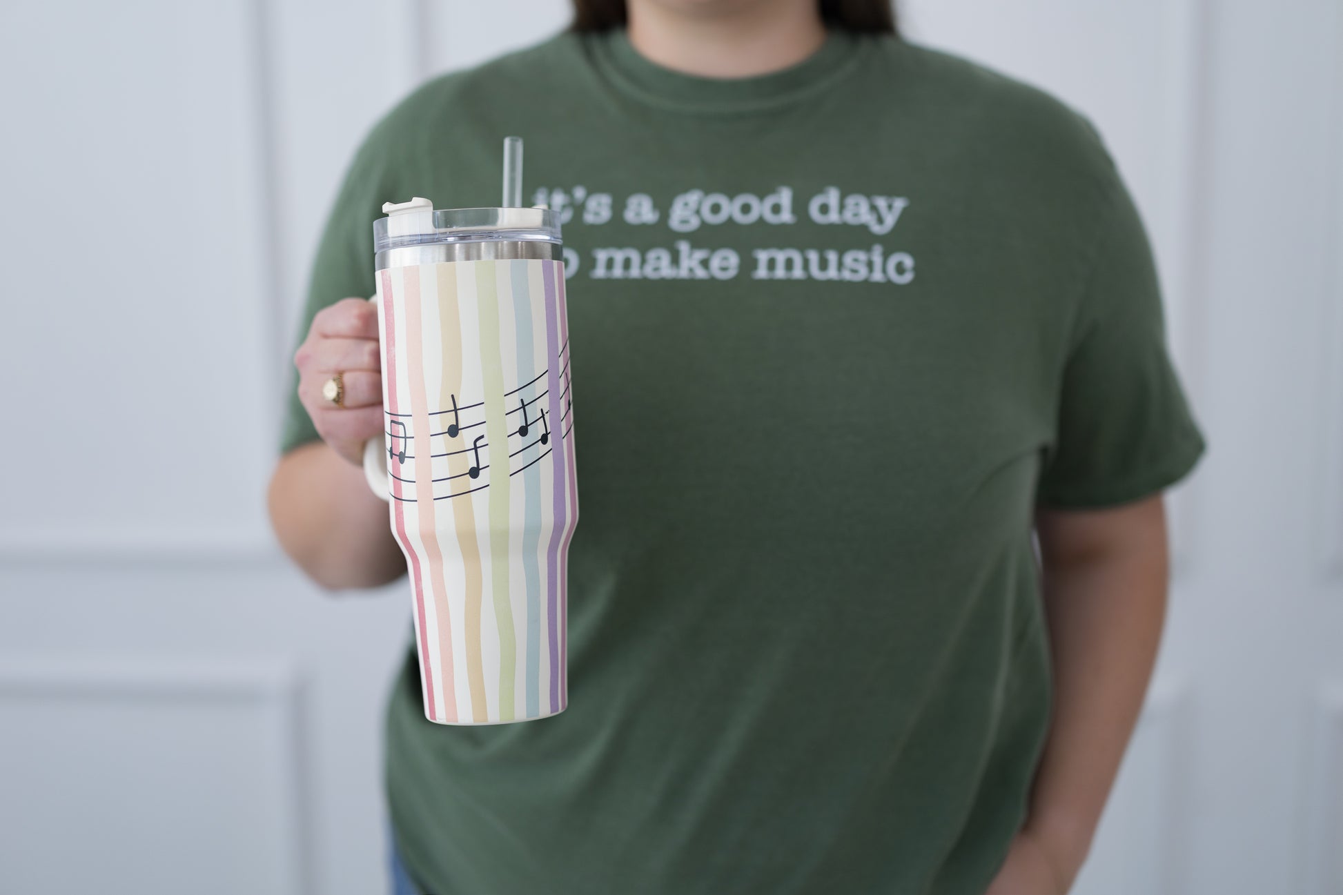 Person wearing a green t-shirt with text holding a striped tumbler.