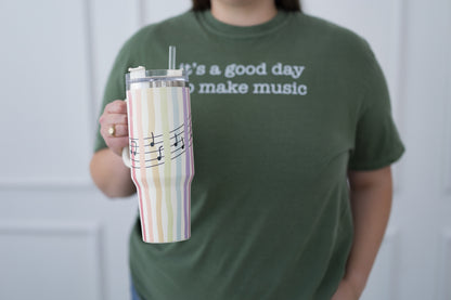 Person wearing a green t-shirt with text holding a striped tumbler.