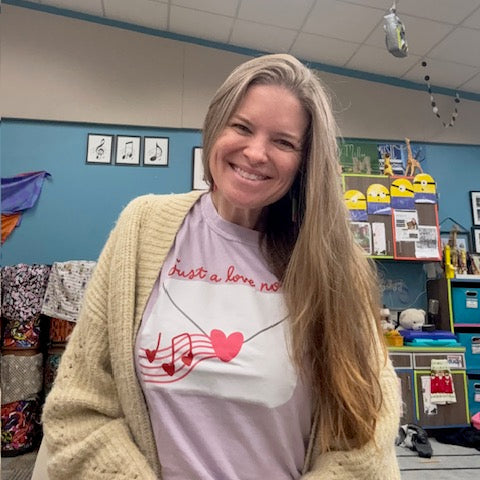 Woman wearing a light-colored sweater over a shirt with a heart design in an indoor setting.
