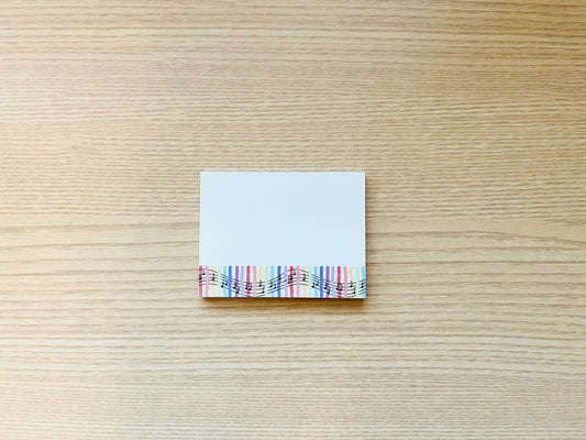 Small square of paper with colorful music notes on a wooden surface