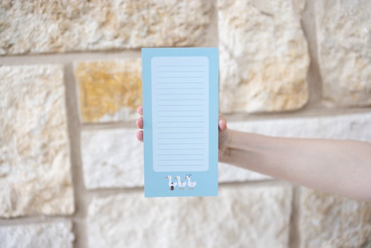 Hand holding a blue notepad with a minimalistic design against a stone wall background