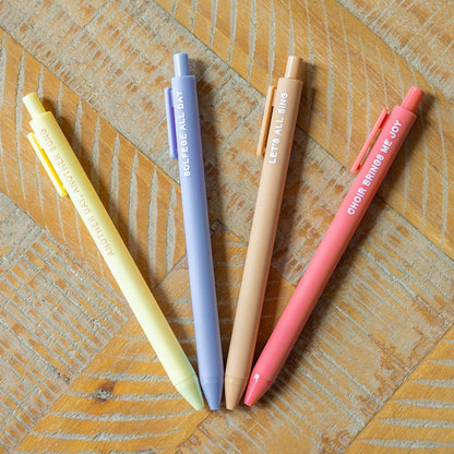 Four pastel-colored pens in yellow, blue, beige, and pink arranged in a fan shape on a wooden surface.